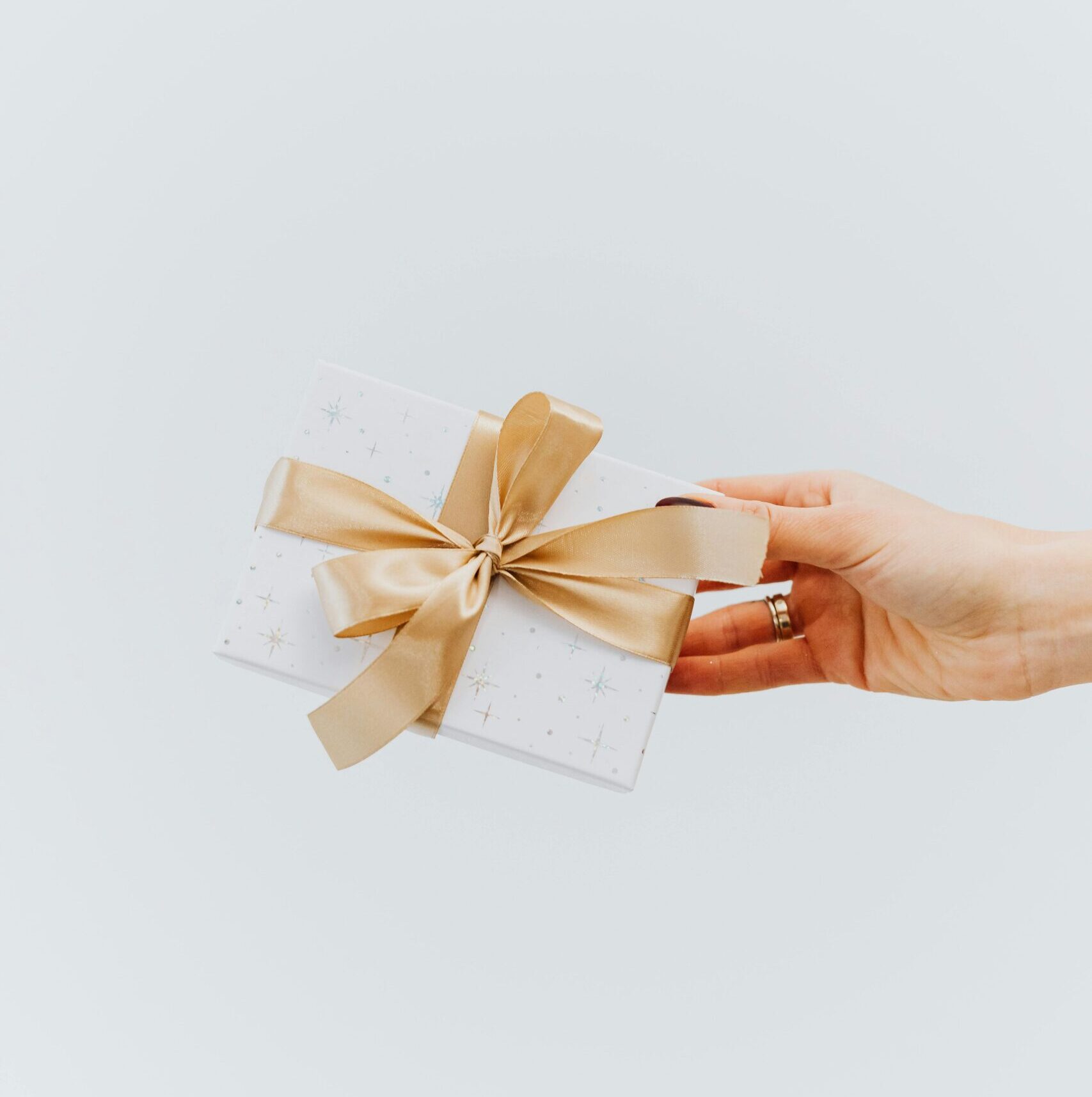 A hand holding an elegantly wrapped gift box with a gold ribbon on a white background.