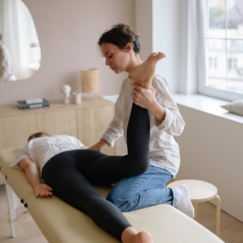 Physiotherapist aiding a woman with leg exercises on a massage table for relaxation and therapy.